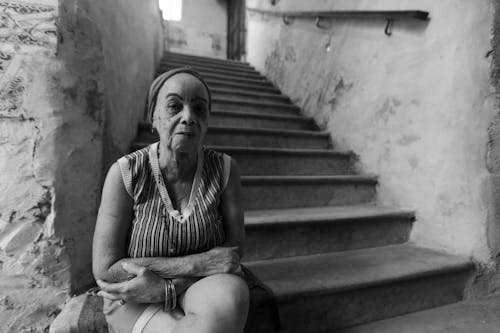 Grayscale Photo of an Elderly Woman Sitting on a Staircase