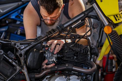 Free Mechanic focused on repairing a motorcycle engine in garage setting. Stock Photo
