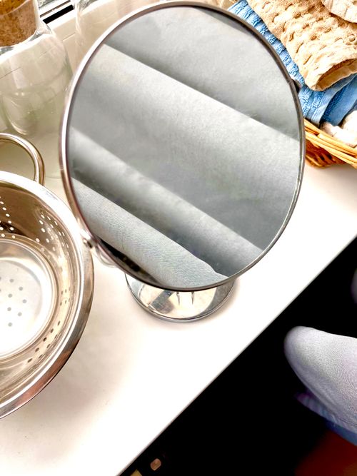 Free Round mirror on a kitchen counter next to a colander and woven basket, depicting a household scene. Stock Photo
