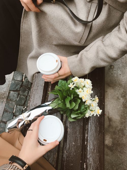 Free Two people holding coffee cups with a bouquet on a bench. Casual and cozy vibe. Stock Photo