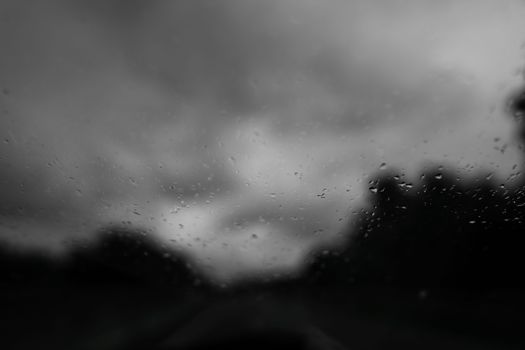 Black and white image of raindrops on glass with stormy clouds, conveying a moody atmosphere.