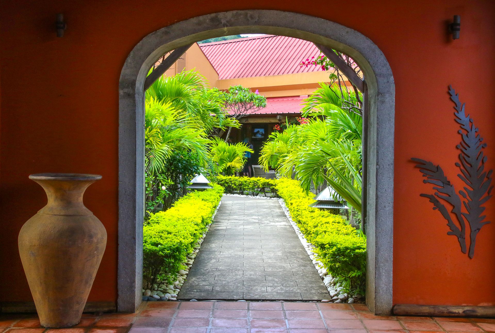 Inviting garden path view through an arched entrance with lush greenery and clay vase.