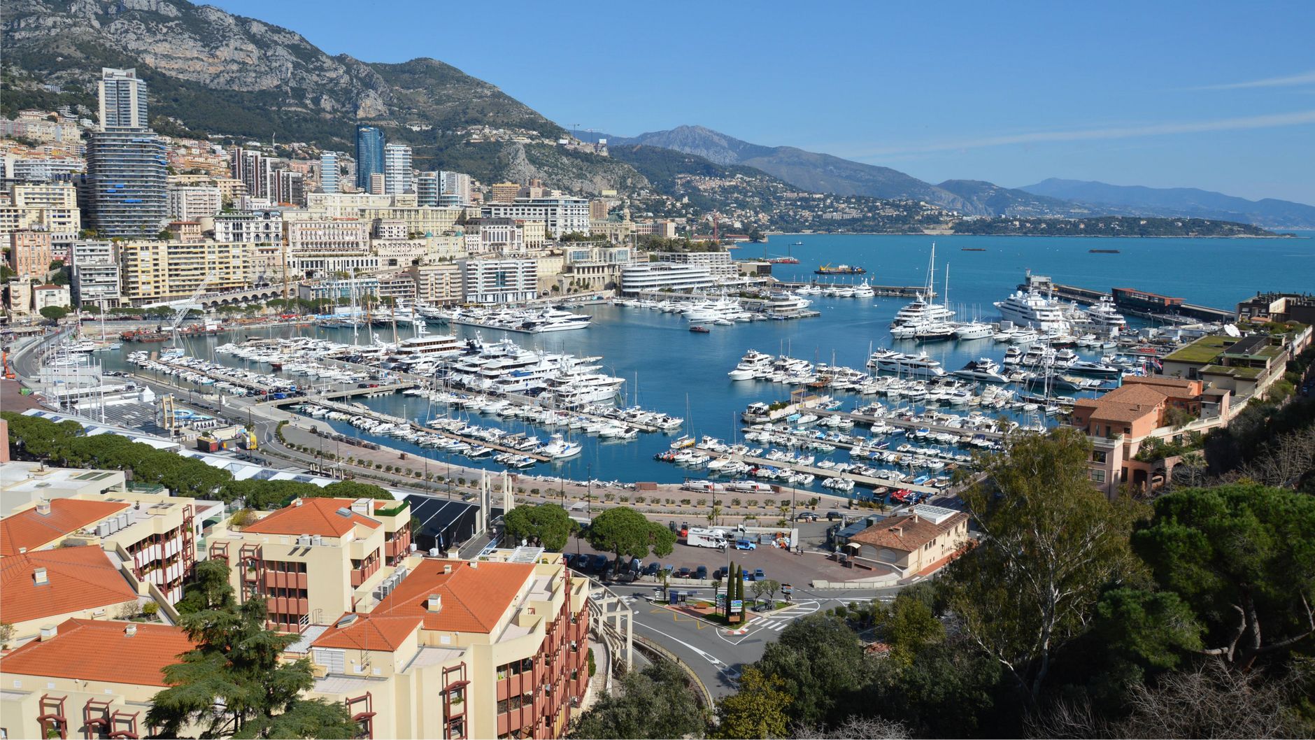 A stunning aerial view of Port Hercules with yachts in Monaco, framed by the cityscape and mountains.
