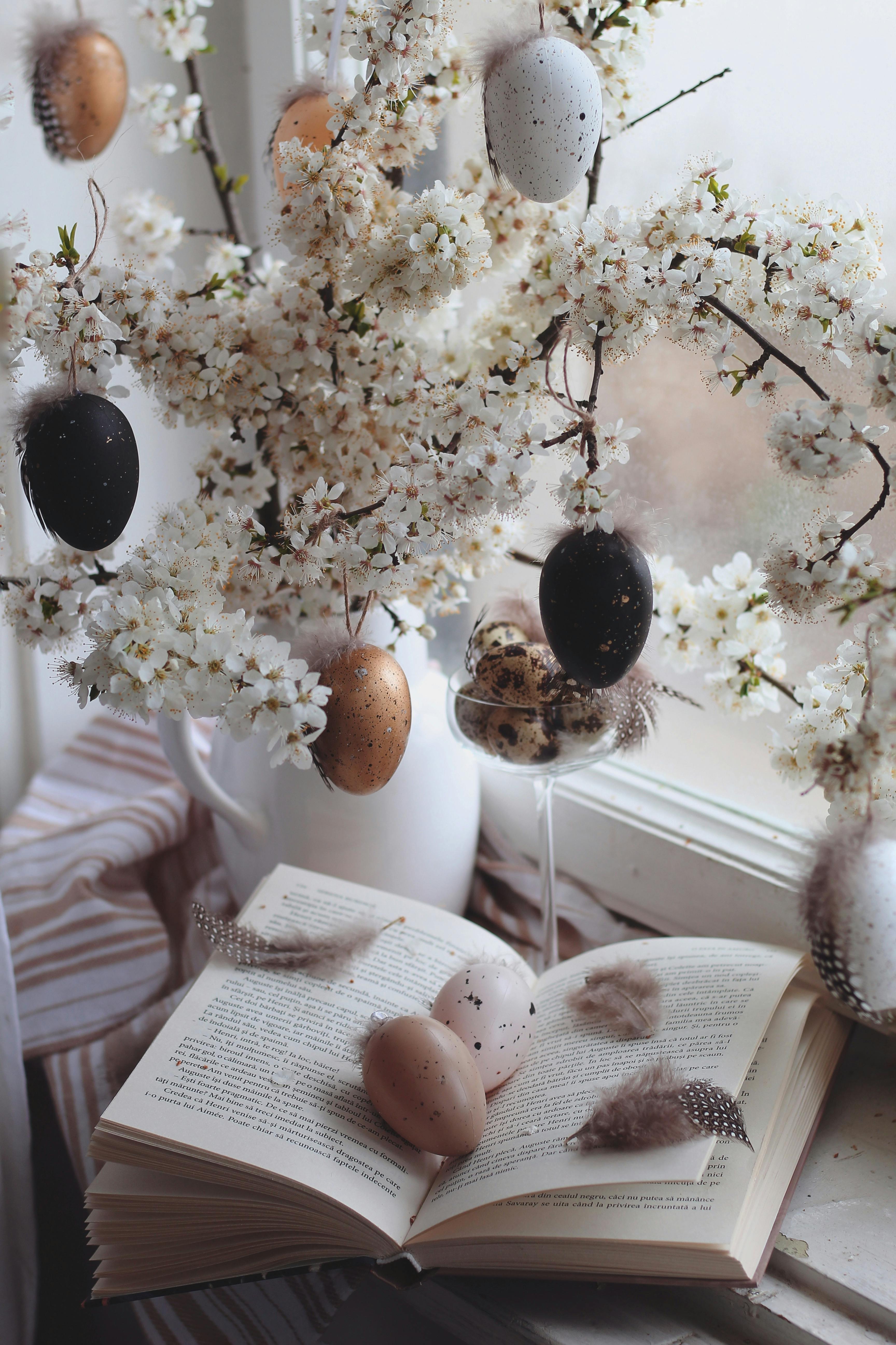 Easter-themed setup with cherry blossoms, decorated eggs, and an open book by a window.