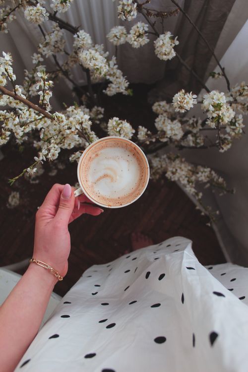Free Elegant top-down view of a woman holding a cappuccino with white floral backdrop. Stock Photo