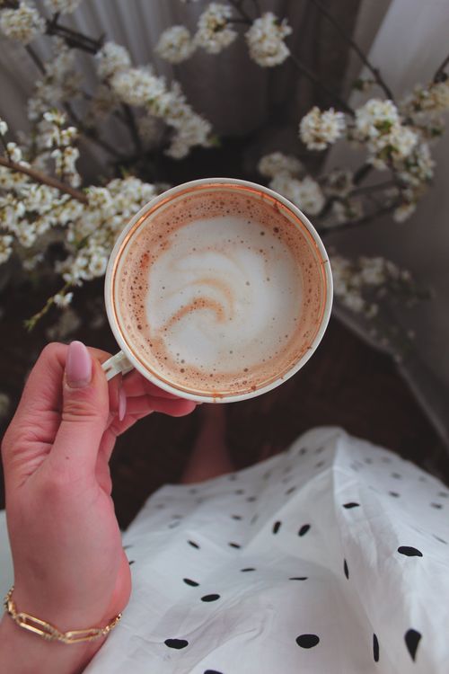 Free A hand holding a cappuccino cup above a floral background. Elegant and calming. Stock Photo