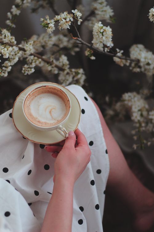 Free Close-up of a hand holding a cappuccino among spring blossoms. Stock Photo