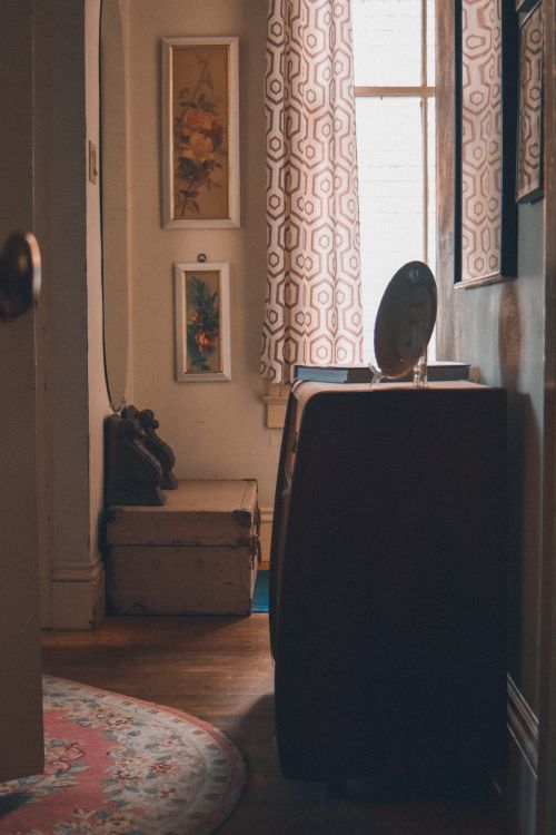 Free Warm vintage hallway interior featuring a cabinet, mirror, floral rug, and patterned curtains. Stock Photo