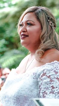 A joyful bride with blonde hair smiling in a white lace dress outdoors at her wedding.
