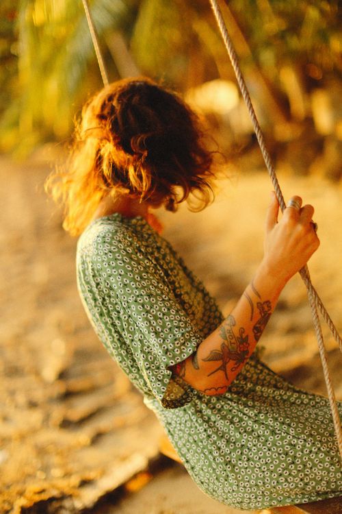 Free A woman with tattoos in a floral dress enjoys a swing at sunset, surrounded by warm tones and nature. Stock Photo