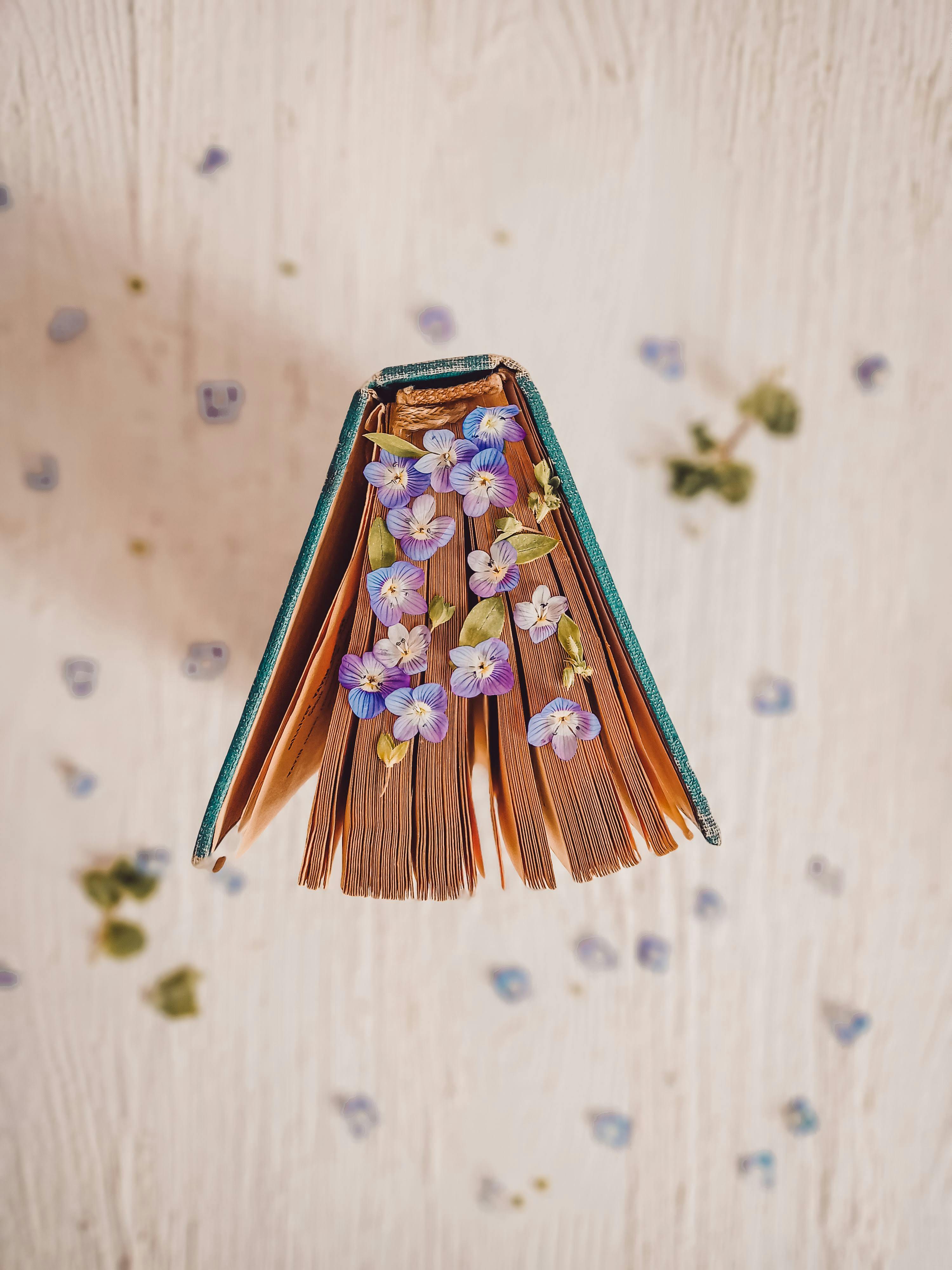 Open book with purple flowers between pages on a white surface, creating an artistic and serene composition.