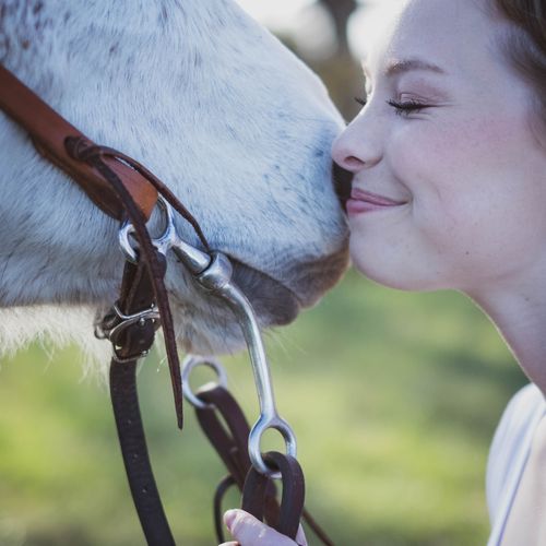 Free A young woman sharing a tender moment with a white horse outdoors on a sunny day. Stock Photo