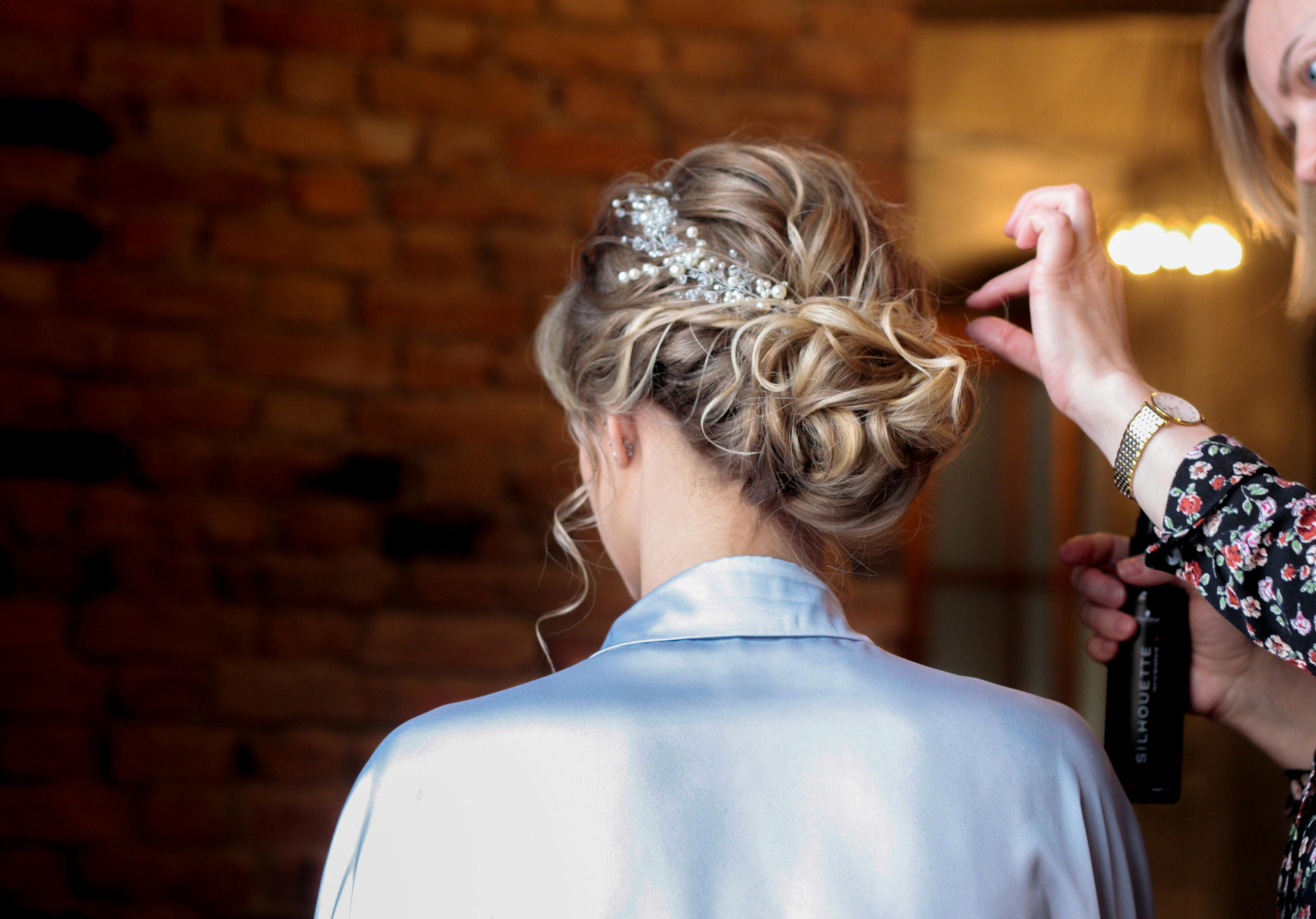 Bridal hairstyling with intricate updo and headpiece being perfected for the wedding day.