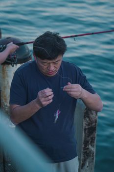 Adult male fisherman preparing his fishing line on a pier in Melbourne, Australia.