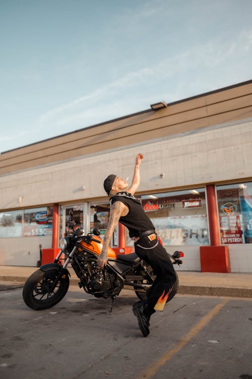 Free Man Standing on Tip Toes with his Arms Raised next to a Motorcycle Stock Photo