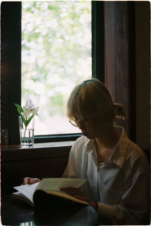 Photo of a Woman Reading a Book Near a Window