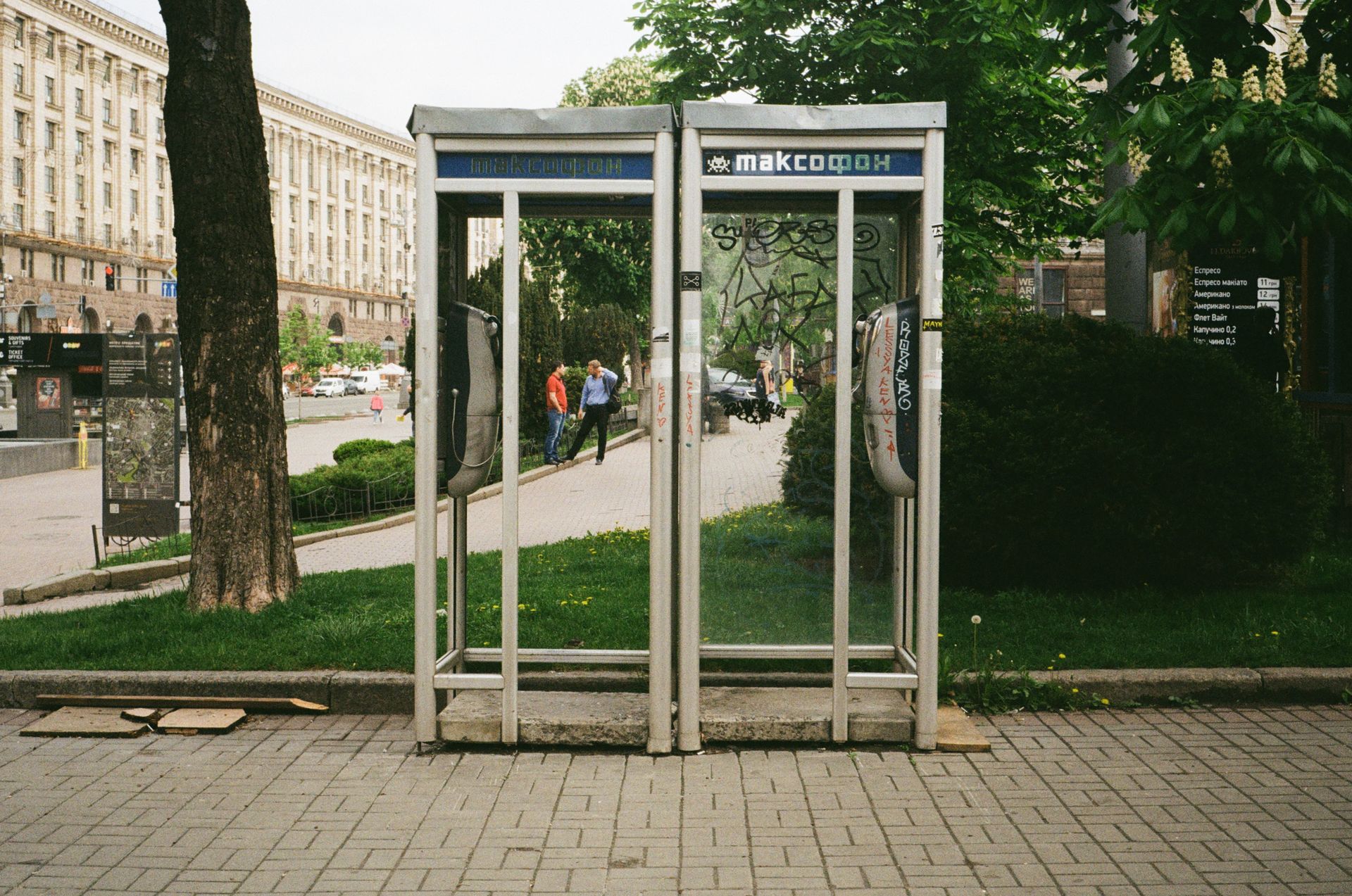 A classic glass telephone booth with graffiti in Kyiv, Ukraine, amidst urban architecture.