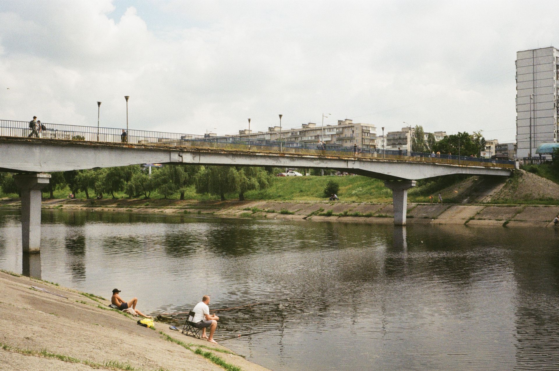Urban landscape in Kyiv featuring a bridge, river, and people by the water.