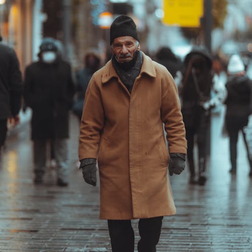 Photo of an Elderly Man in a Brown Coat Walking on a Street