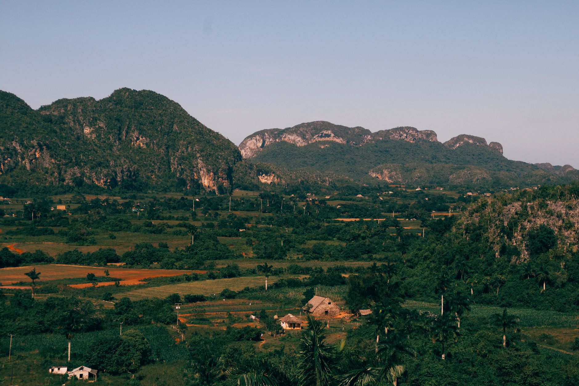A stunning aerial view of the lush green countryside and mountains in Cuba, under a clear sky.