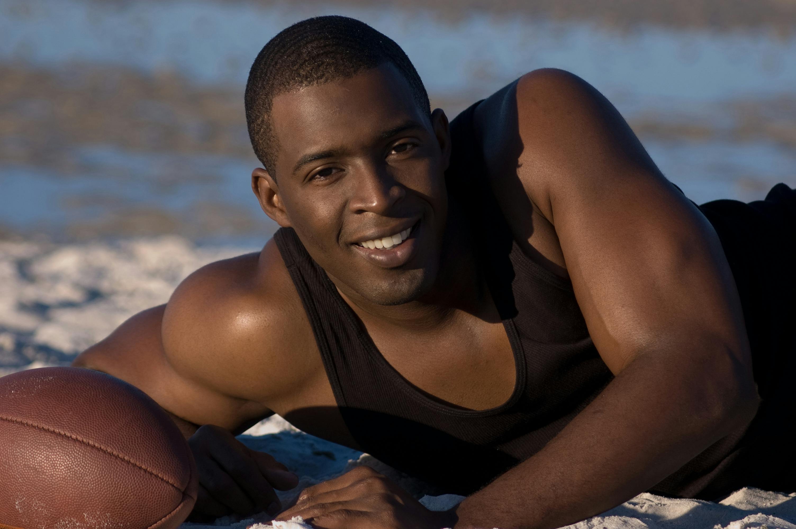 photo of a man in a black tank top smiling near a football