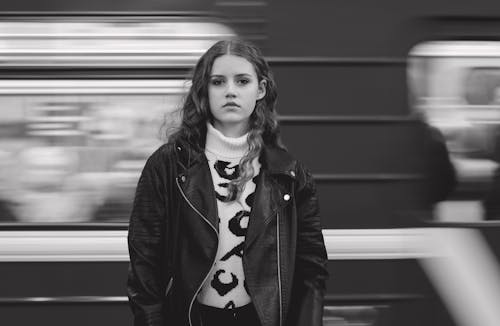 Grayscale Photo of a Woman Standing Near a Moving Train