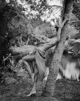 Artistic monochrome photo of a woman posing gracefully by a tree in Thai nature.