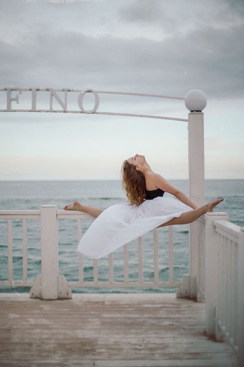 Free A ballet dancer elegantly performs a split on a beachside railing, showcasing grace and flexibility. Stock Photo