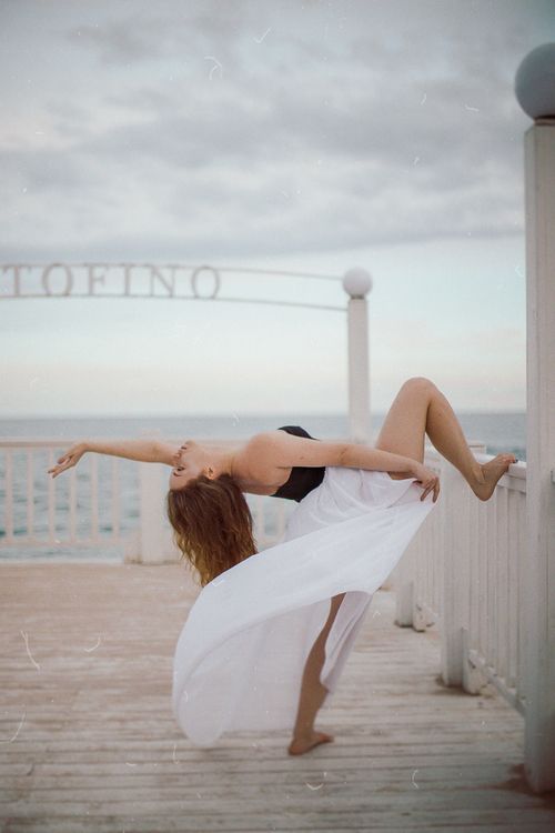 Free A woman in a graceful pose on an oceanfront pier, capturing elegance and movement. Stock Photo
