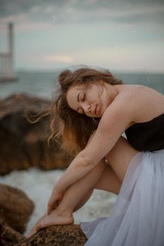 Woman with closed eyes sitting on rocks by the sea, exuding calm and tranquility.