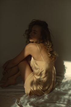 Elegant woman in silk dress sits in sunlight, creating a warm, intimate mood.