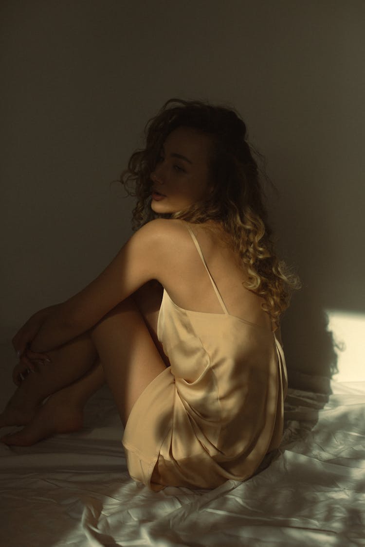 Woman In A Nude Silk Dress Sitting On Bed 
