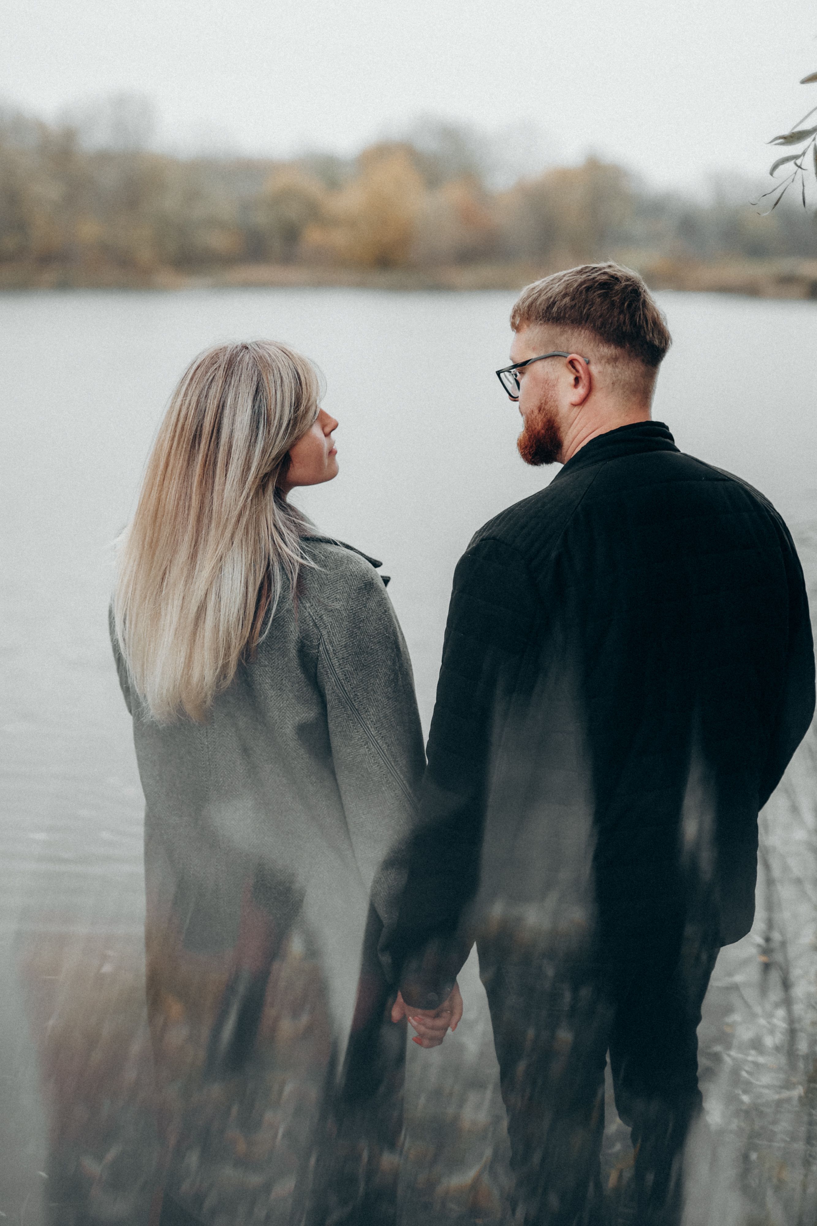 A couple standing by a serene lake, holding hands in a romantic moment.