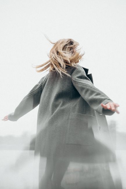 A woman enjoys the freedom of an open field with arms outstretched and hair blown by the wind.