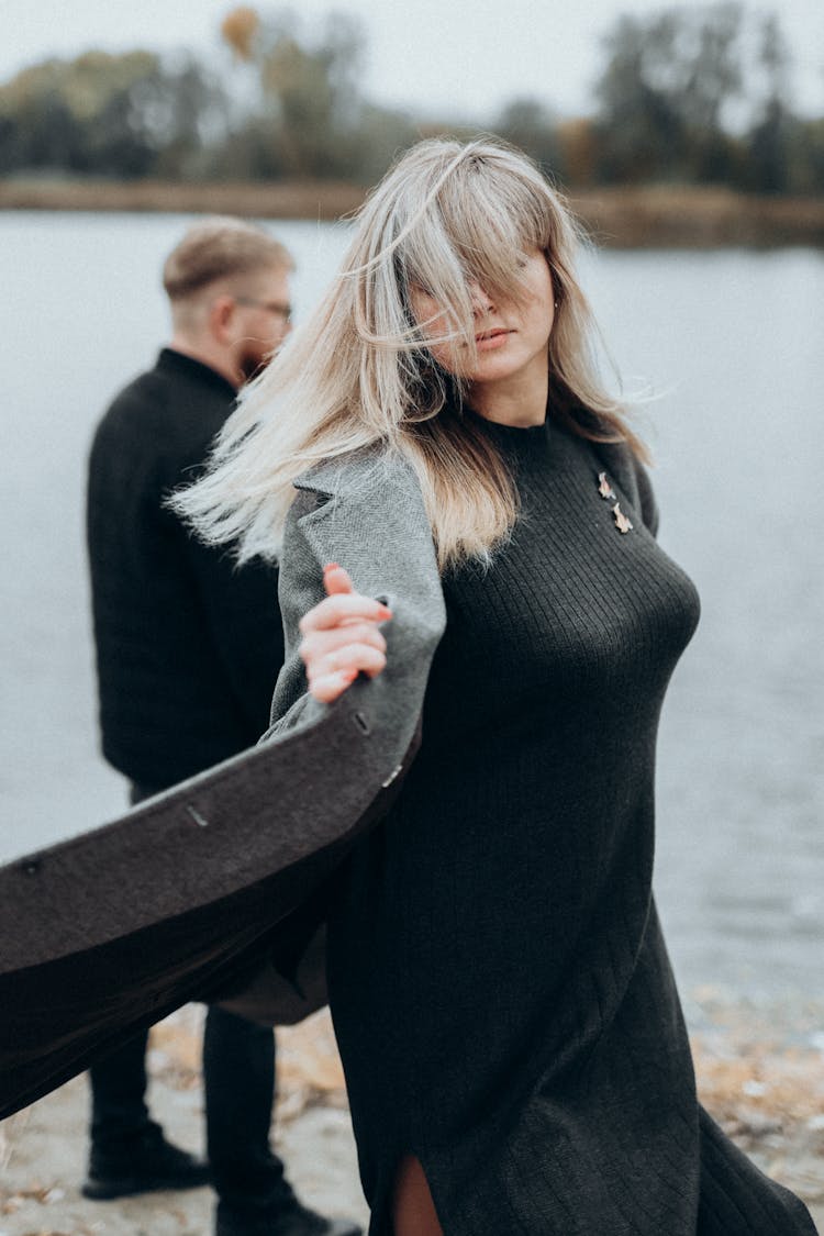 Woman Walking Towards The Camera In The Wind And Man Standing Behind Her 