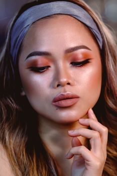 Close-up portrait of an Asian woman showcasing elegant makeup and nude lips.