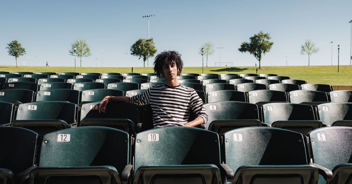 A lone athlete sitting on a bench, head down, with an empty stadium behind them