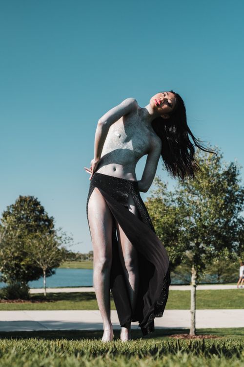 Free A woman in an artistic pose outdoors surrounded by nature under a clear sky. Stock Photo