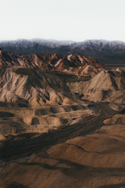 Sweeping aerial shot of rugged, arid mountain landscape with snowcapped peaks.