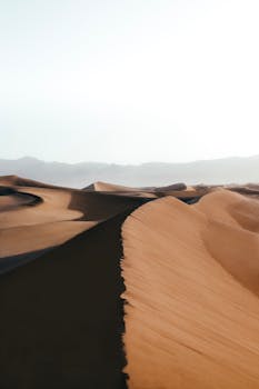 Breathtaking view of windswept sand dunes and distant hills under a clear sky.