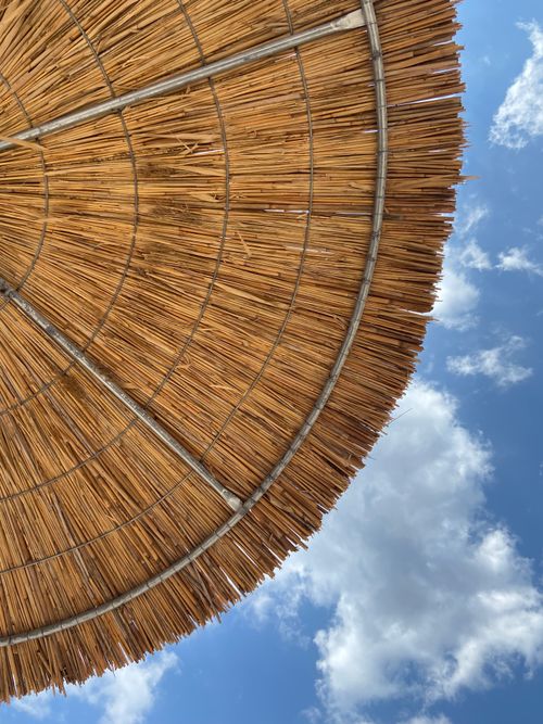Free Low angle view of a woven parasol against a clear blue sky with clouds. Stock Photo