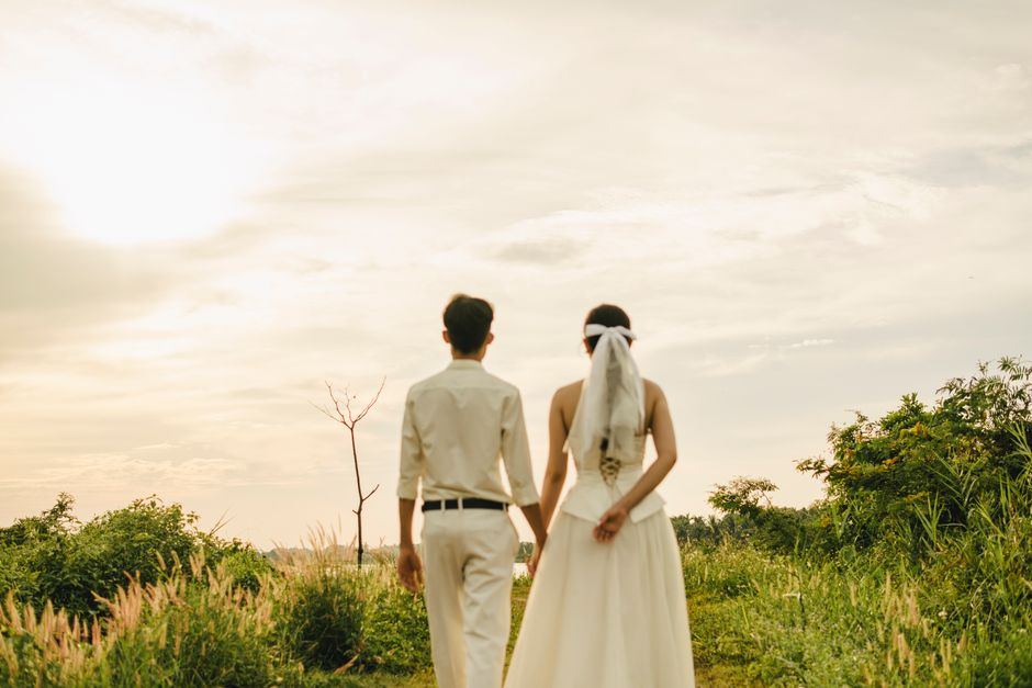 Bride and groom holding hands, walking through a sunny field.