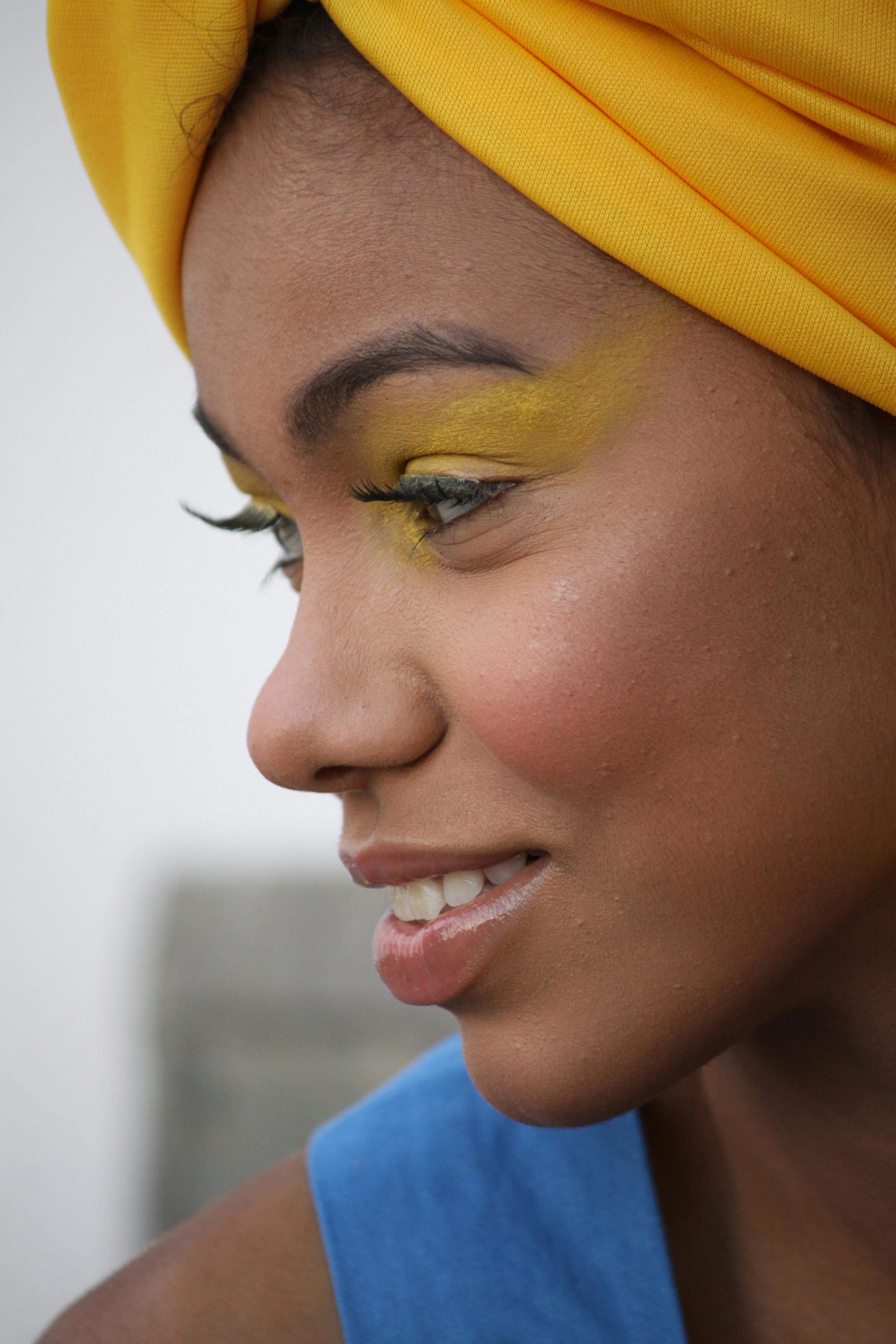 Close-up portrait of a woman with vibrant yellow makeup and headscarf, smiling gently.