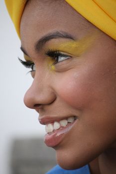 Side profile of a young woman smiling, wearing yellow eyeshadow and headwrap.