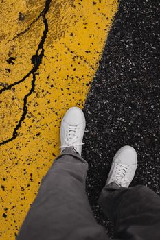 Person wearing white sneakers stands on cracked yellow road marking. Urban style.