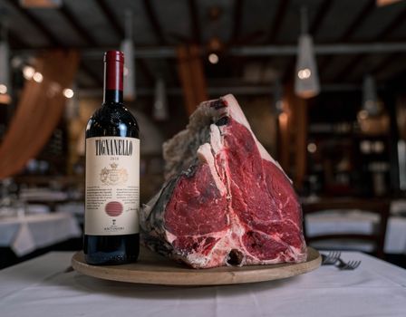 A luxurious pairing of raw steak with a bottle of premium red wine on a restaurant table.