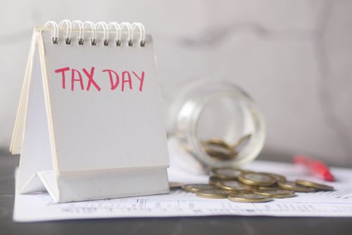 Free A close-up of a table calendar marked 'Tax Day' with a jar of coins and notes, symbolizing financial planning. Stock Photo