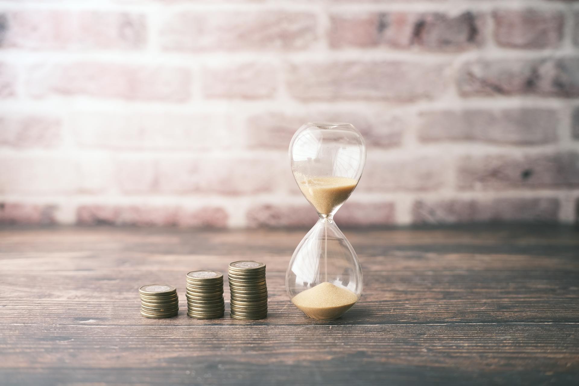 Hourglass and stacked coins on wood, symbolizing the concept of time and money.