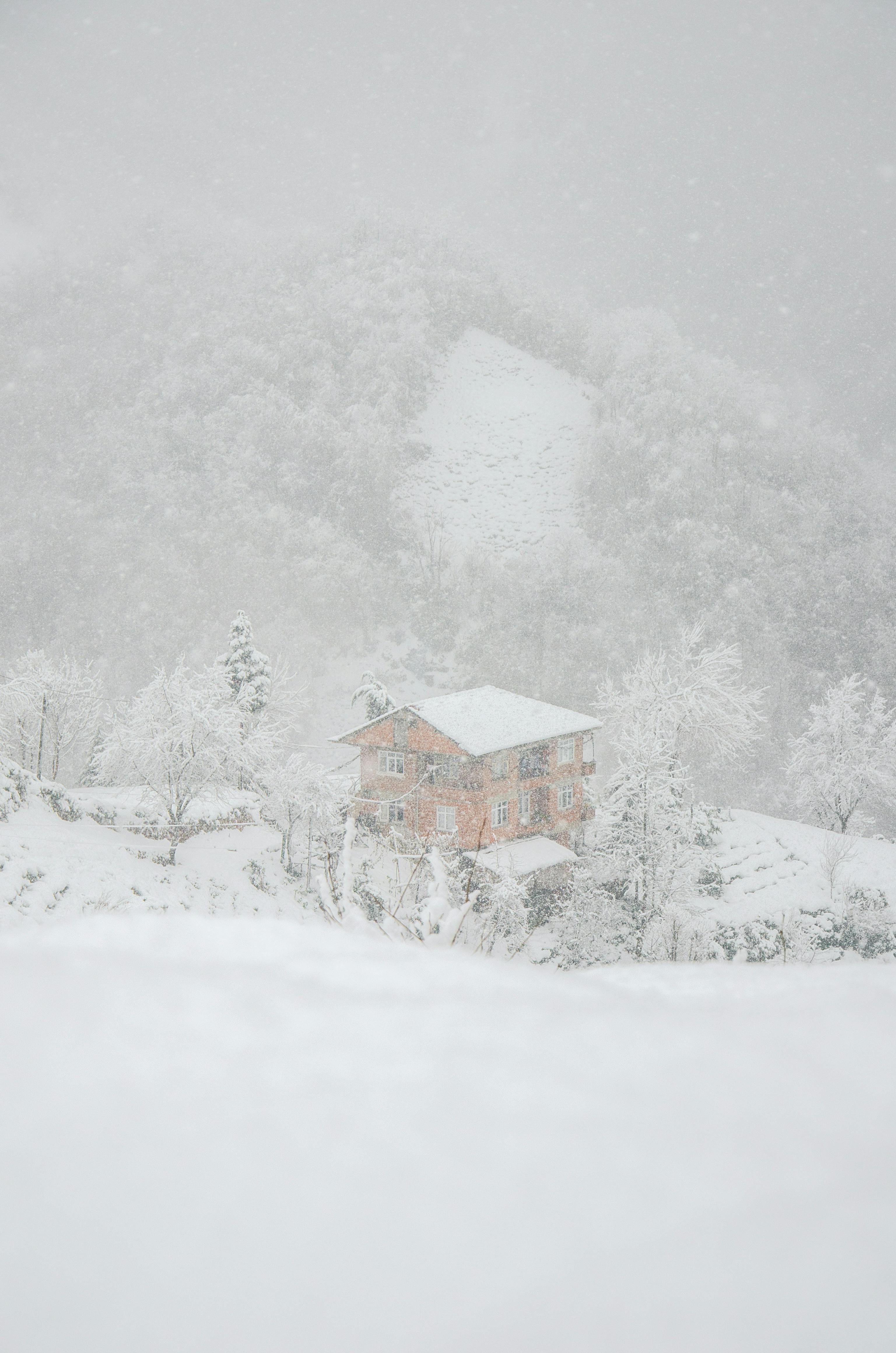 Peaceful winter scene of a house blanketed in snow amidst a serene mountain backdrop.