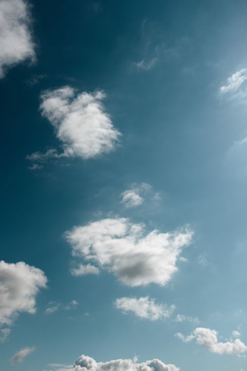 Free Fluffy white clouds float in a clear blue sky, conveying a serene atmosphere. Stock Photo